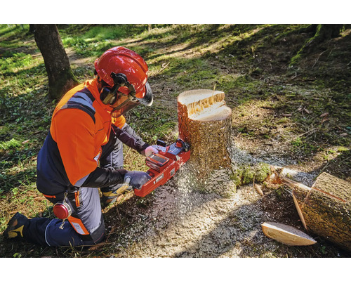 Une personne portant un équipement de protection utilise une tronçonneuse sur une souche d''arbre.