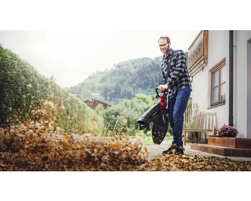 Mann verwendet einen Laubsauger zur Gartenarbeit vor einem Haus.