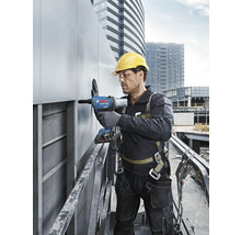 Un homme portant un casque de protection et un harnais de sécurité utilise une riveteuse sur un chantier.