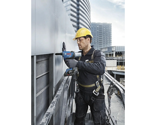 Un homme portant un casque de protection et un harnais de sécurité utilise une riveteuse sur un chantier.