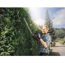 Mann schneidet Hecke mit einer Heckenschere im Garten.