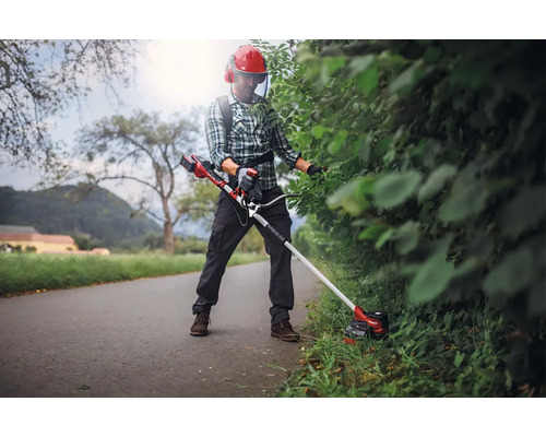 Personne taillant une haie avec un coupe-bordures à batterie et des vêtements de protection