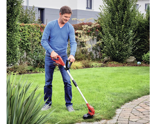 Un homme utilise un coupe-bordure dans un jardin avec une pelouse.