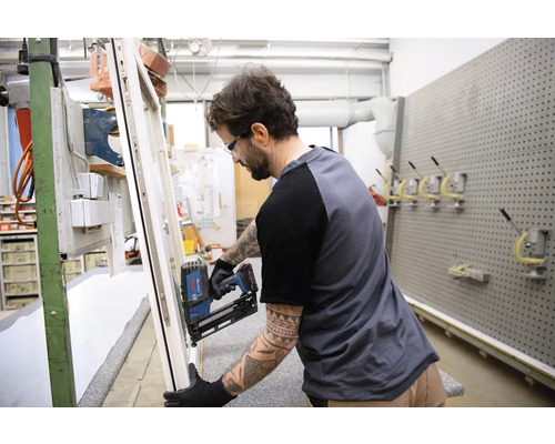 Ein Handwerker befestigt mit einem Nagelgerät ein Fenster in einer Werkstatt.