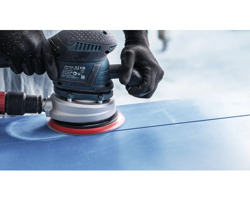 Ein Mann schleift eine blaue Oberfläche mit einem Exzenterschleifer.