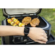 Barbecue avec des aliments et une montre intelligente au poignet