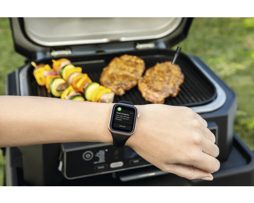 Grill mit Grillgut und Smartwatch am Handgelenk