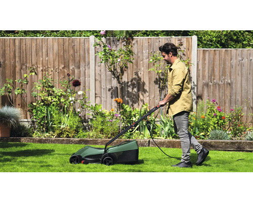 Un homme tond la pelouse avec une tondeuse à gazon électrique dans un jardin.