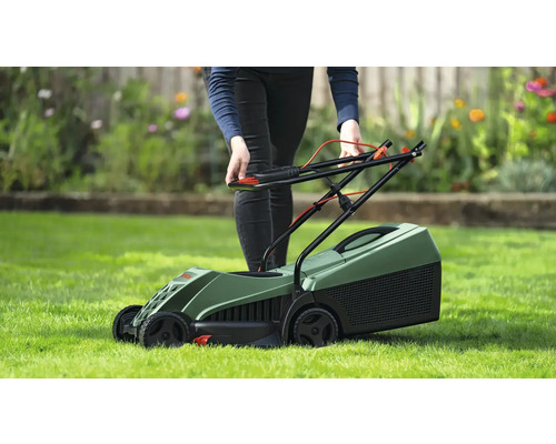 Une personne utilise une tondeuse à gazon verte sur une pelouse.