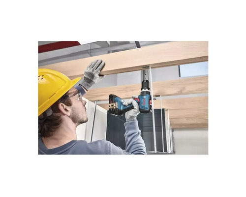 Un artisan portant un casque de sécurité perce une planche de bois sur une construction de plafond avec une perceuse sans fil.