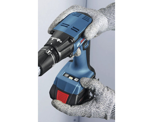 Une personne gantée tient une visseuse sans fil pour cloisons sèches.