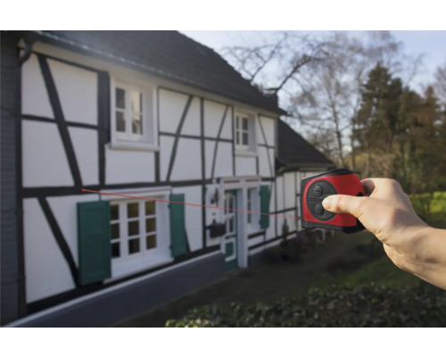 Une main utilise un télémètre laser sur une maison à colombages