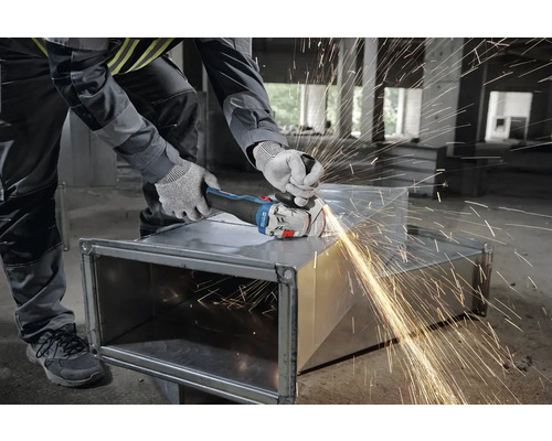 Un artisan meule du métal avec une meuleuse d'angle, des étincelles jaillissent.