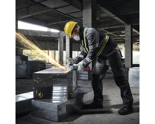 Un homme portant un casque de sécurité meule du métal avec une meuleuse d'angle, ce qui provoque des étincelles.