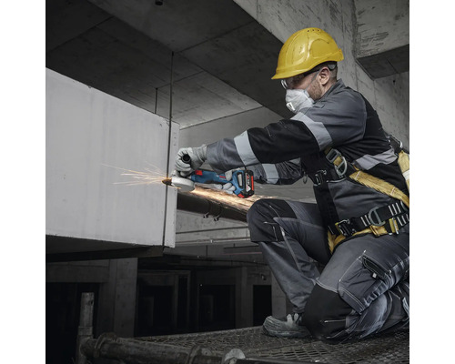 Artisan avec casque de protection, lunettes de sécurité et masque respiratoire travaillant avec une meuleuse d'angle sans fil.