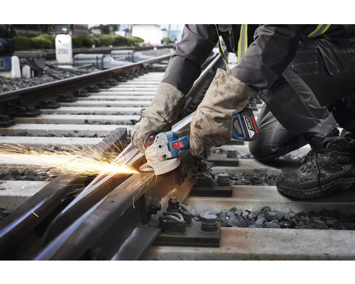 Un ouvrier coupe un rail de chemin de fer avec une meuleuse d'angle, produisant des étincelles.