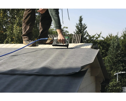 Handwerker befestigt Dachpappe mit einem Drucklufttacker auf einem Dach.