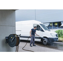 Une personne nettoie un véhicule avec un tuyau d''arrosage relié à un enrouleur de tuyau.