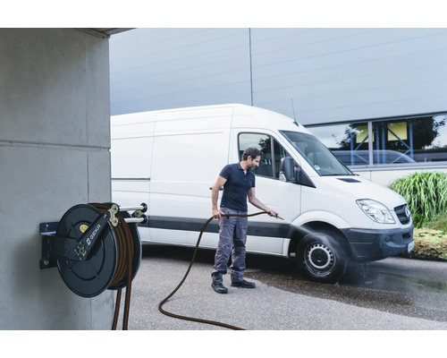 Une personne nettoie un véhicule avec un tuyau d''arrosage relié à un enrouleur de tuyau.