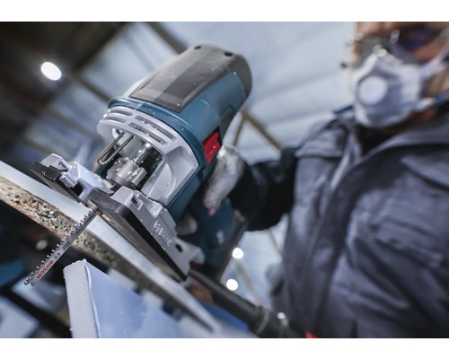 Une scie sauteuse coupe une pièce, utilisée par une personne portant des vêtements de protection.
