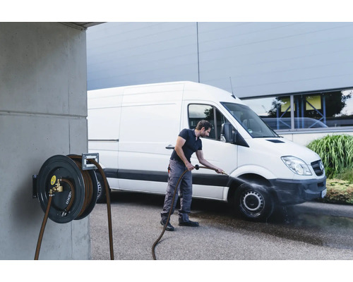 Mann reinigt Transporter mit einer Schlauchtrommel an einer Betonwand