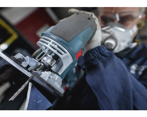 Une scie sauteuse en cours d''utilisation pour couper un matériau, manipulée par une personne portant un masque de protection et des lunettes de sécurité.