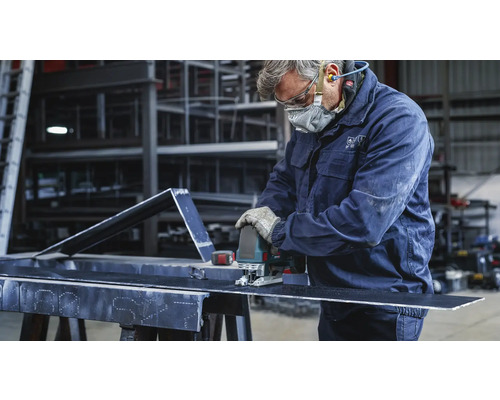 Un artisan coupe une pièce métallique avec une scie sauteuse. Il porte des vêtements de protection.