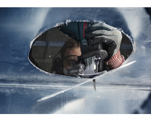 Gros plan d''une personne portant des lunettes de protection en train de découper un trou dans une plaque de métal avec une scie sauteuse.