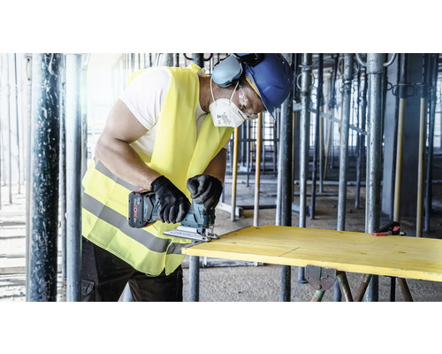Un artisan scie une planche de bois avec une scie sauteuse sans fil sur un chantier.