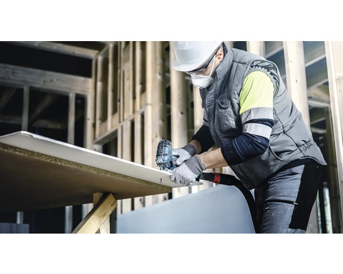 Un ouvrier coupe une plaque de plâtre avec une scie sauteuse sur un chantier