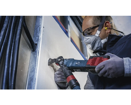 Un artisan découpe une ouverture dans une plaque de plâtre à l''aide d''un outil multifonction.