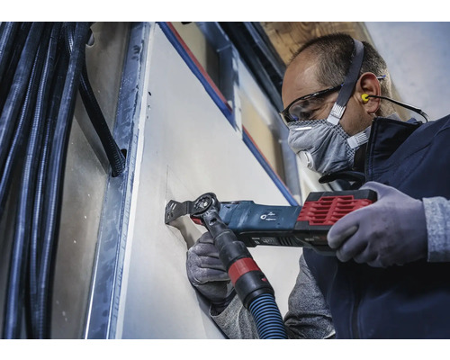 Un artisan découpe un trou dans une plaque de plâtre avec un outil multifonction