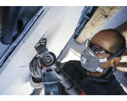 Artisan travaillant avec un outil multifonctionnel sur un plafond, équipé de lunettes de protection et d''un masque antipoussière