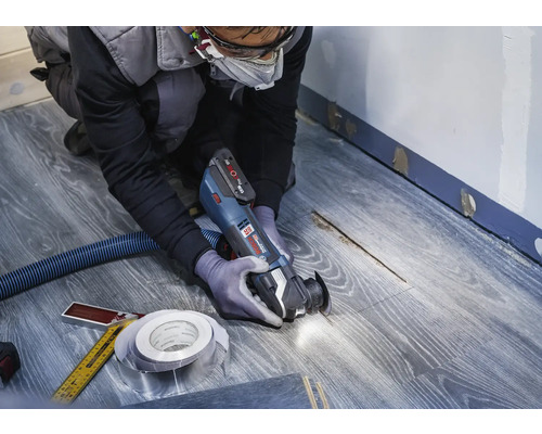 Artisan utilisant un outil multifonction sur un sol stratifié pour des travaux de rénovation.