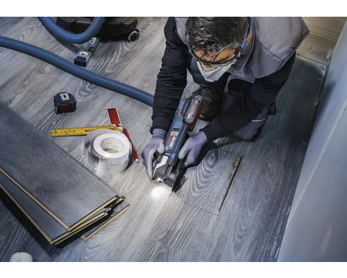 Un artisan coupe du stratifié avec une machine-outil multifonctionnelle pour créer une découpe pour un tuyau. Des outils tels qu''un mètre ruban et un crayon sont à portée de main.