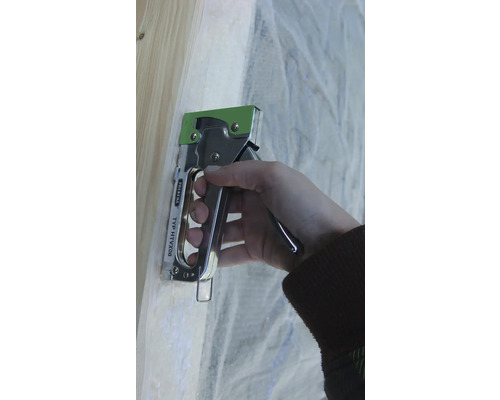 Eine Hand bedient einen Handtacker an einem Holzrahmen, um Folie zu befestigen.