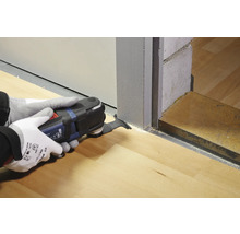 Une personne utilise un outil multifonction pour travailler un chambranle de porte sur un plancher en bois.