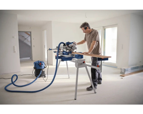 Un homme coupe du bois avec une scie à onglet dans une pièce lumineuse
