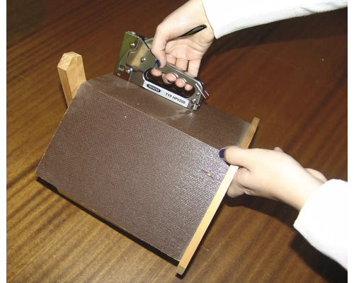 Une personne fixe un morceau de tissu sur une construction en bois avec une agrafeuse.