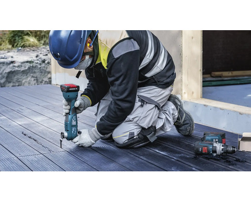 Un ouvrier utilise un outil multifonctionnel sur une terrasse en bois. Des équipements de protection individuelle sont également présents.
