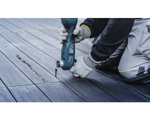 Une personne travaille avec un outil multifonctionnel sur une terrasse en bois.