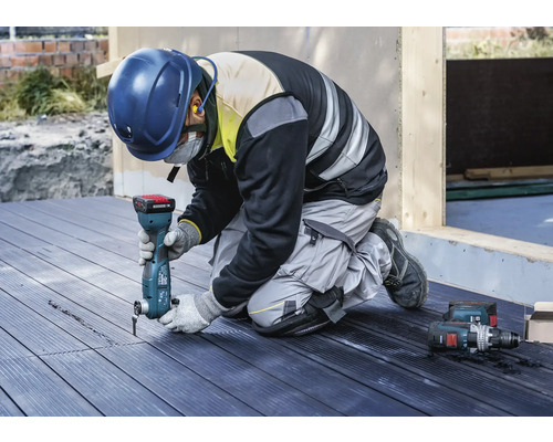 Un artisan est agenouillé sur une terrasse et travaille avec un outil multifonction