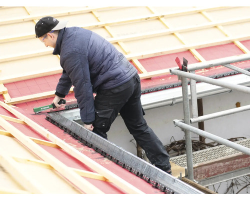 Ein Dachdecker befestigt Vogelschutzgitter auf einem Dach.