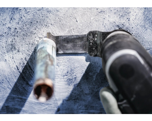 Outil électrique oscillant avec lame de scie à métaux coupant un tuyau métallique.