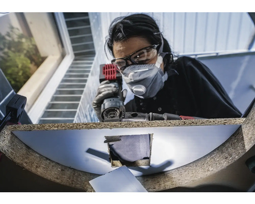 Une femme portant des lunettes de protection et un masque antipoussière travaille sur une pièce à l''aide d''une meuleuse multiple.