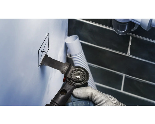 Artisan coupant un trou dans un mur avec un outil multifonction