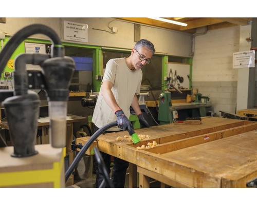 Mann reinigt eine Werkbank mit einem Staubsauger in einer Werkstatt.