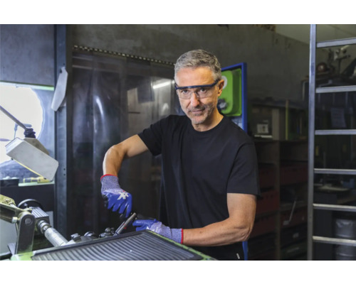 Homme portant des lunettes de protection et des gants de protection travaillant sur une machine dans un atelier.
