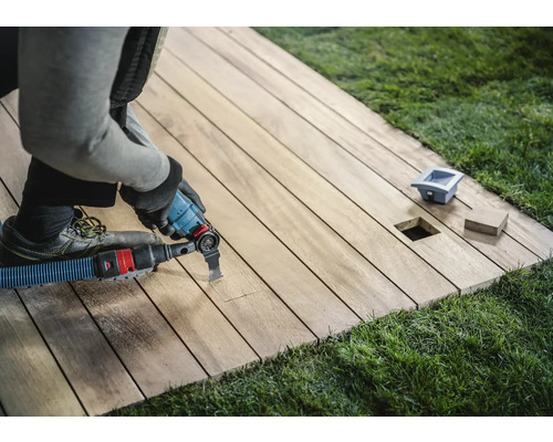 Un artisan travaille sur une terrasse en bois avec un outil multifonction