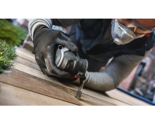 Un homme utilise un outil multifonction avec une lame de scie sur une planche de bois.